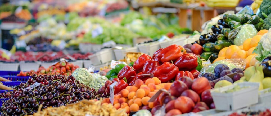 Colorful assortment of fresh fruits and vegetables in a bustling outdoor market scene.