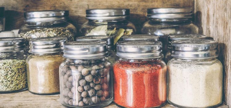 A collection of assorted spices in glass jars on a rustic wooden shelf for culinary use.
